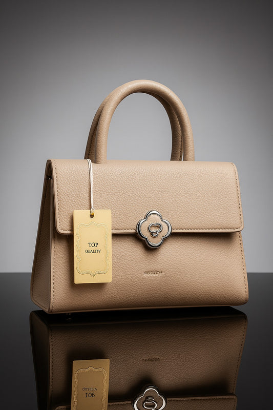 Beige handbag with a gold tag on a reflective surface and gray background