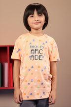 A child wearing a peach-colored graphic jersey t-shirt with retro arcade graphics, including the text 'BACK TO ACADE' and colorful pixelated game characters.