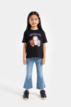 A girl wearing a black T-shirt with graphics and blue flare jeans, standing against a white background.