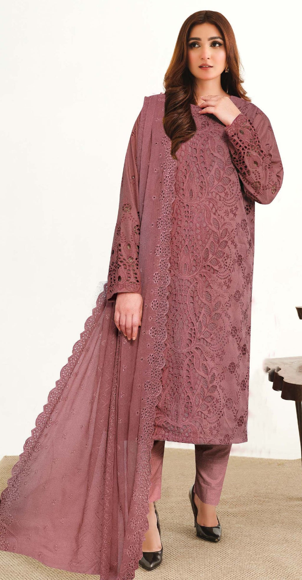 A woman wearing a traditional Pakistani three-piece suit with Chikankari embroidery, consisting of a shirt, pants, and a chiffon dupatta.