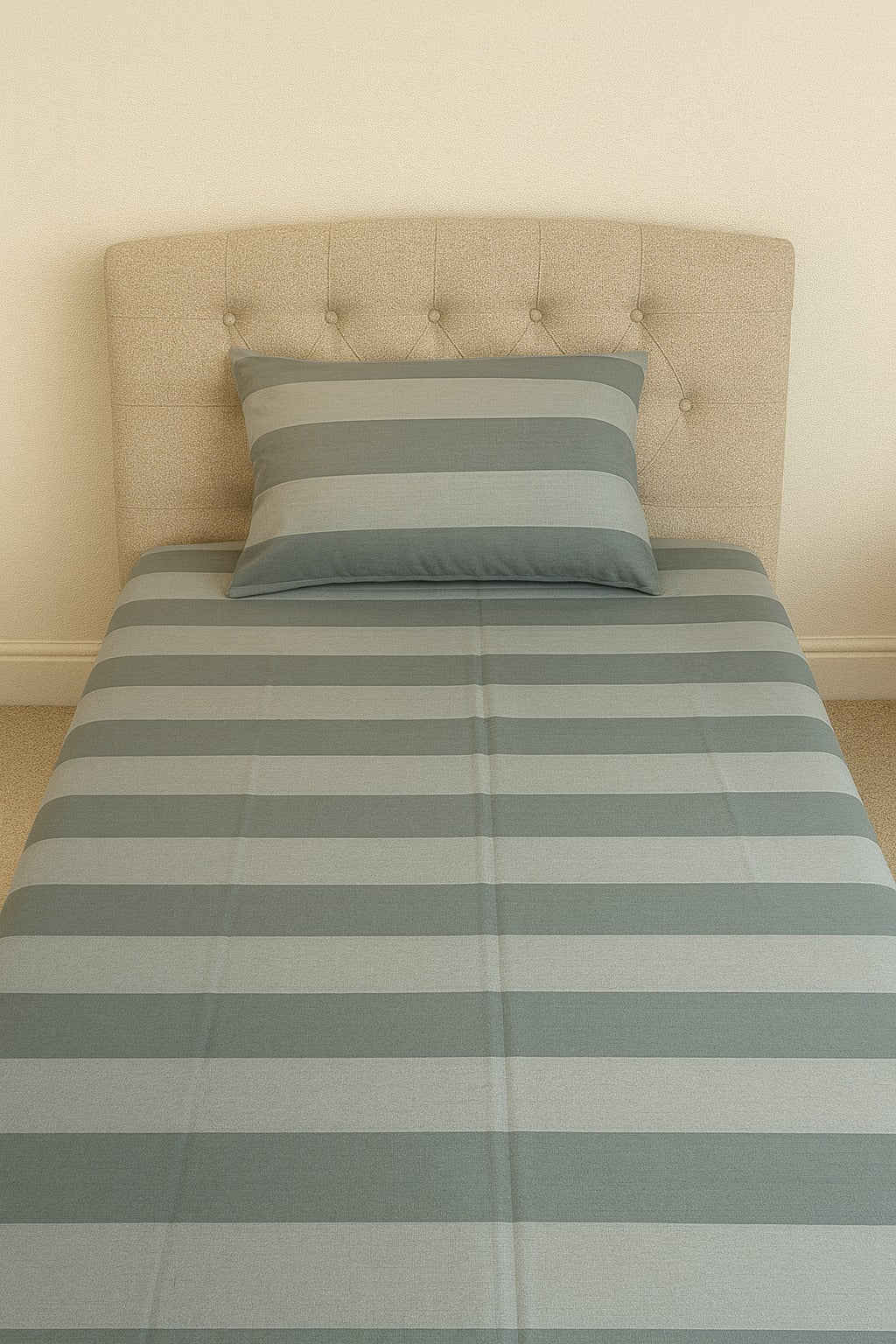 Bedsheet with striped bedding and a pillow against a beige wal