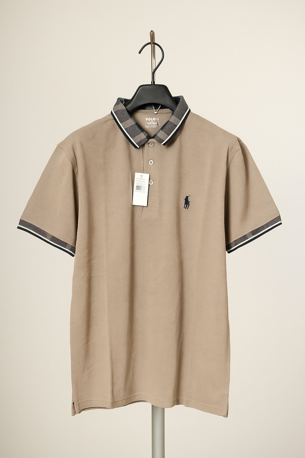 Beige polo shirt with black collar and trim on a hanger against a beige background