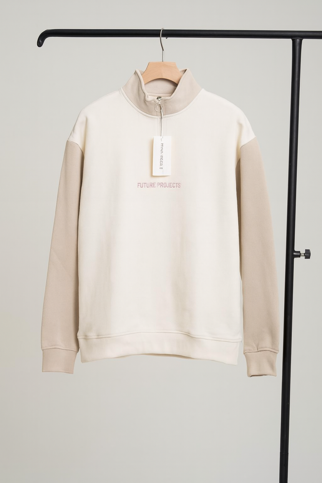 Beige sweatshirt with a tag on a hanger against a gray background