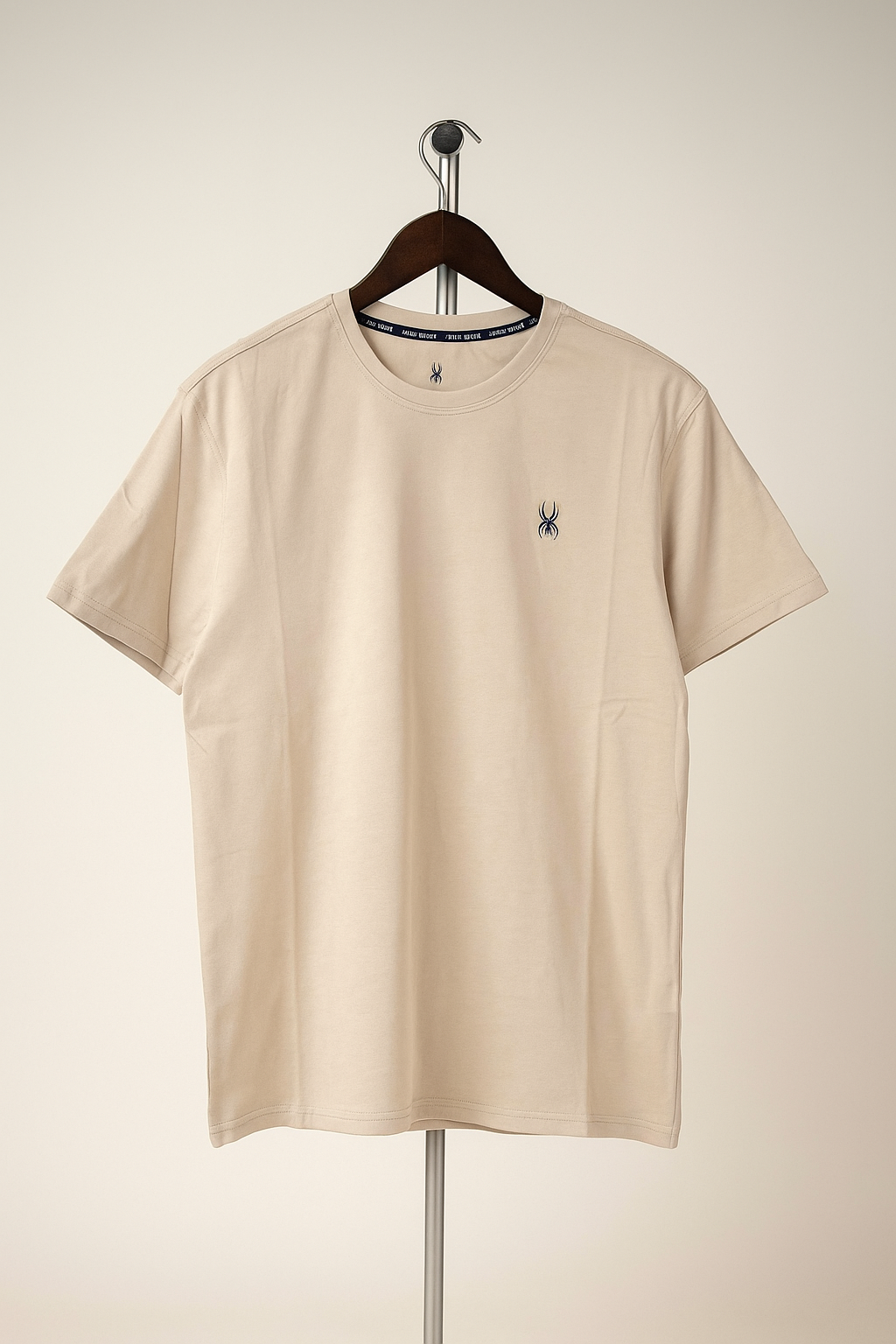 Beige t-shirt with a small logo on a hanger against a beige background
