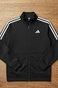 Black Adidas tracksuit jacket with white stripes on a wooden surface