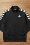 Black Adidas tracksuit jacket with white stripes on a wooden surface