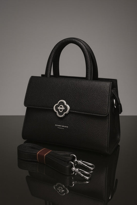 Black handbag with a silver clasp on a reflective surface
