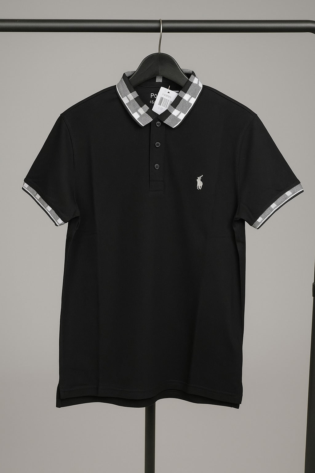 Black polo shirt with plaid collar on a hanger against a gray background