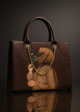 Brown handbag with artistic design of a person holding flowers, on a dark background