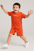 Child wearing an orange DKNY outfit with arms outstretched on a light gray background