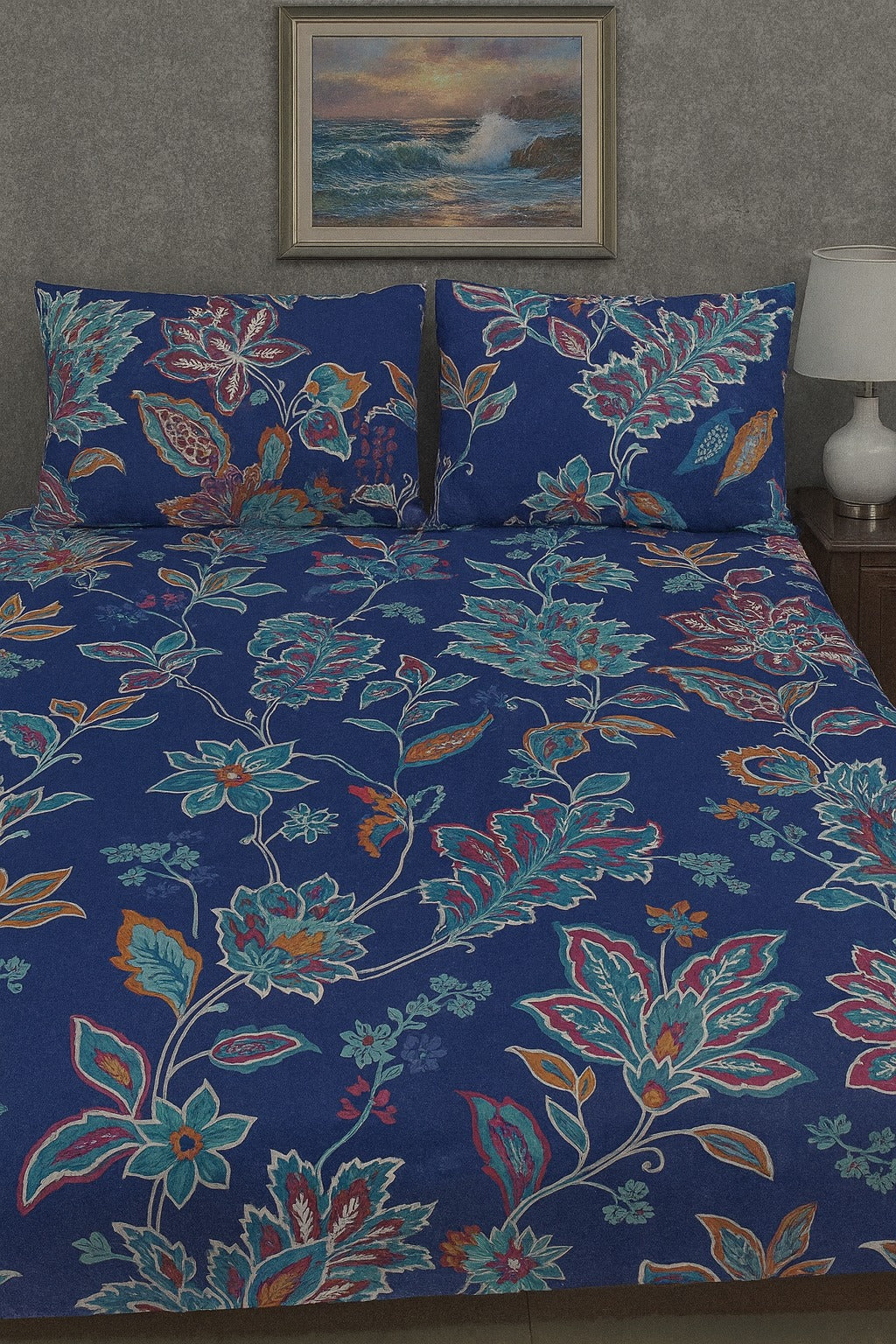 Floral patterned bedspread on a bed with matching pillows, against a wall with a seascape painting.