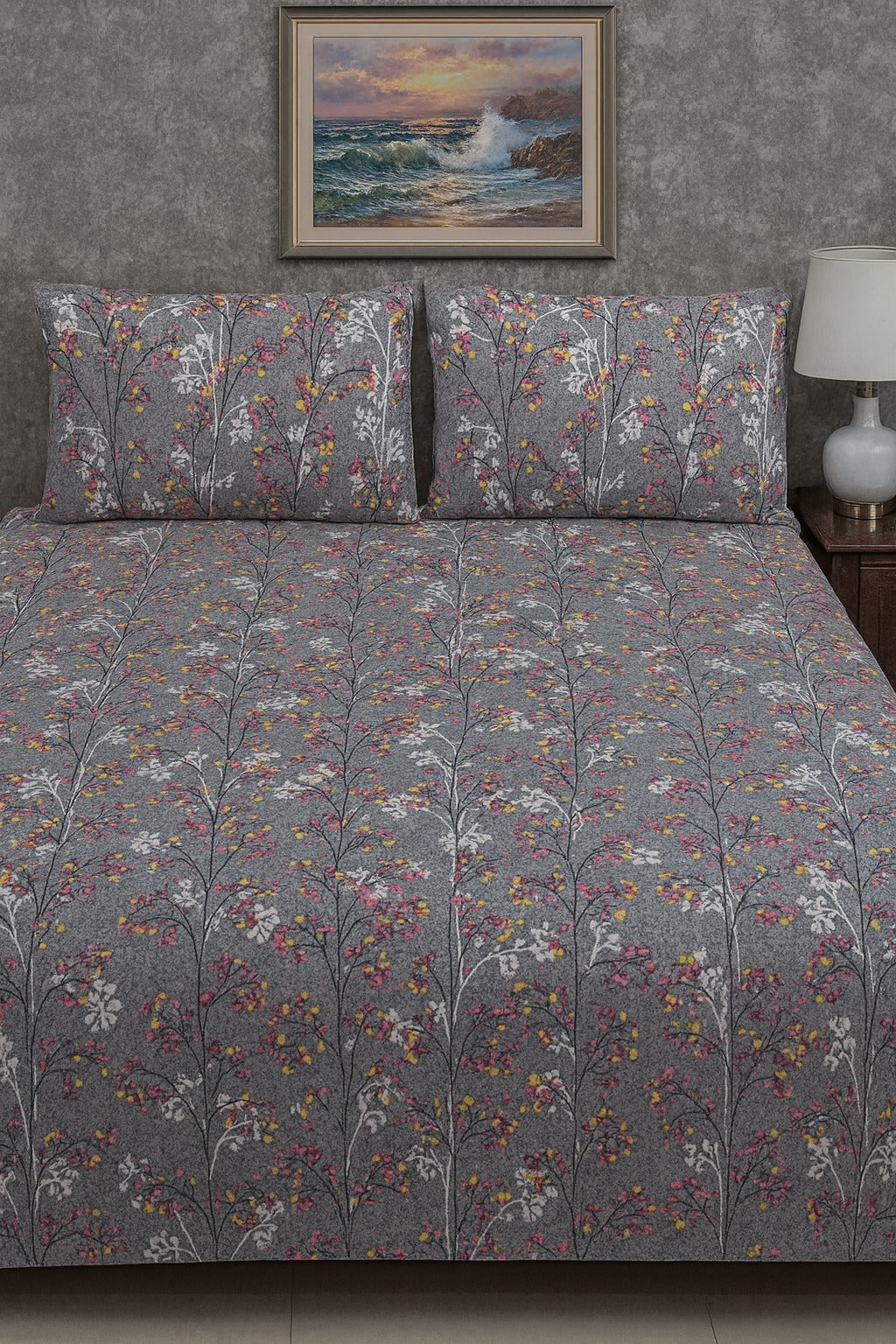 Floral patterned bedspread on a bed with matching pillows, framed artwork above, and a lamp on a nightstand.