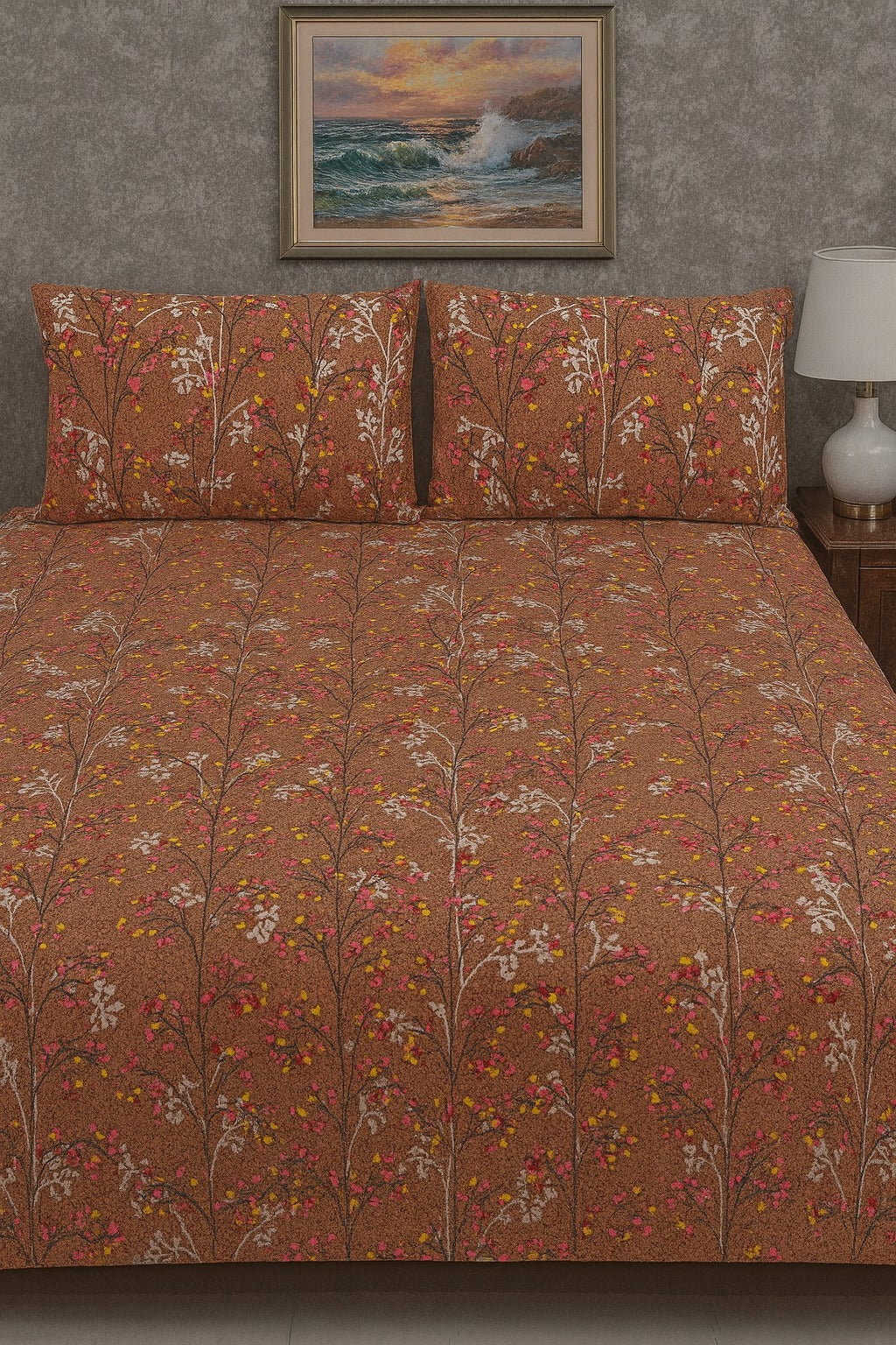 Floral patterned bedspread on a bed with matching pillows, against a wall with a framed picture of a sunset over water.