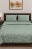 Green patterned bedding set on a bed with a framed picture on the wall.