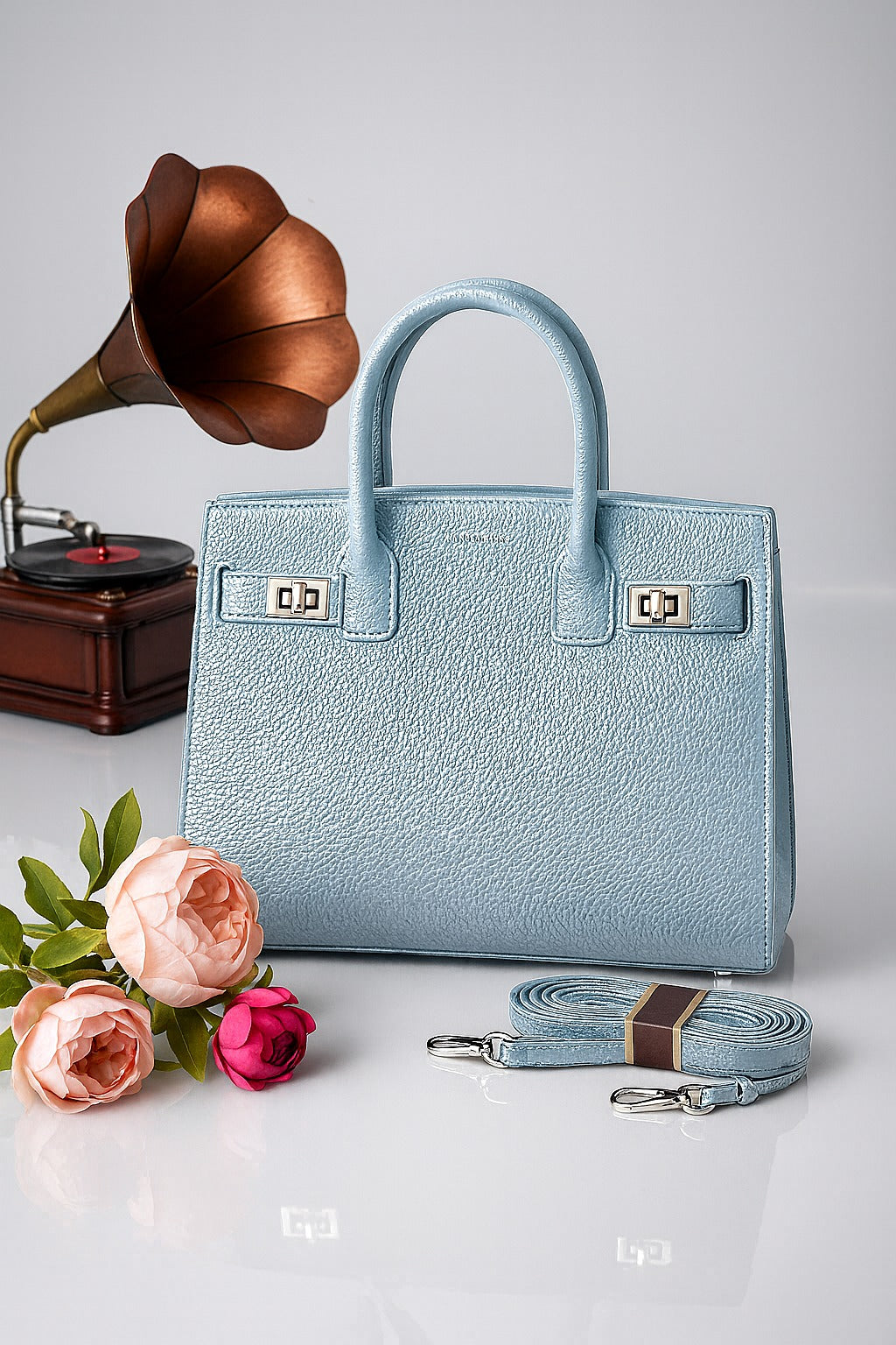 Light blue handbag with matching strap, flowers, and vintage record player on a light gray background