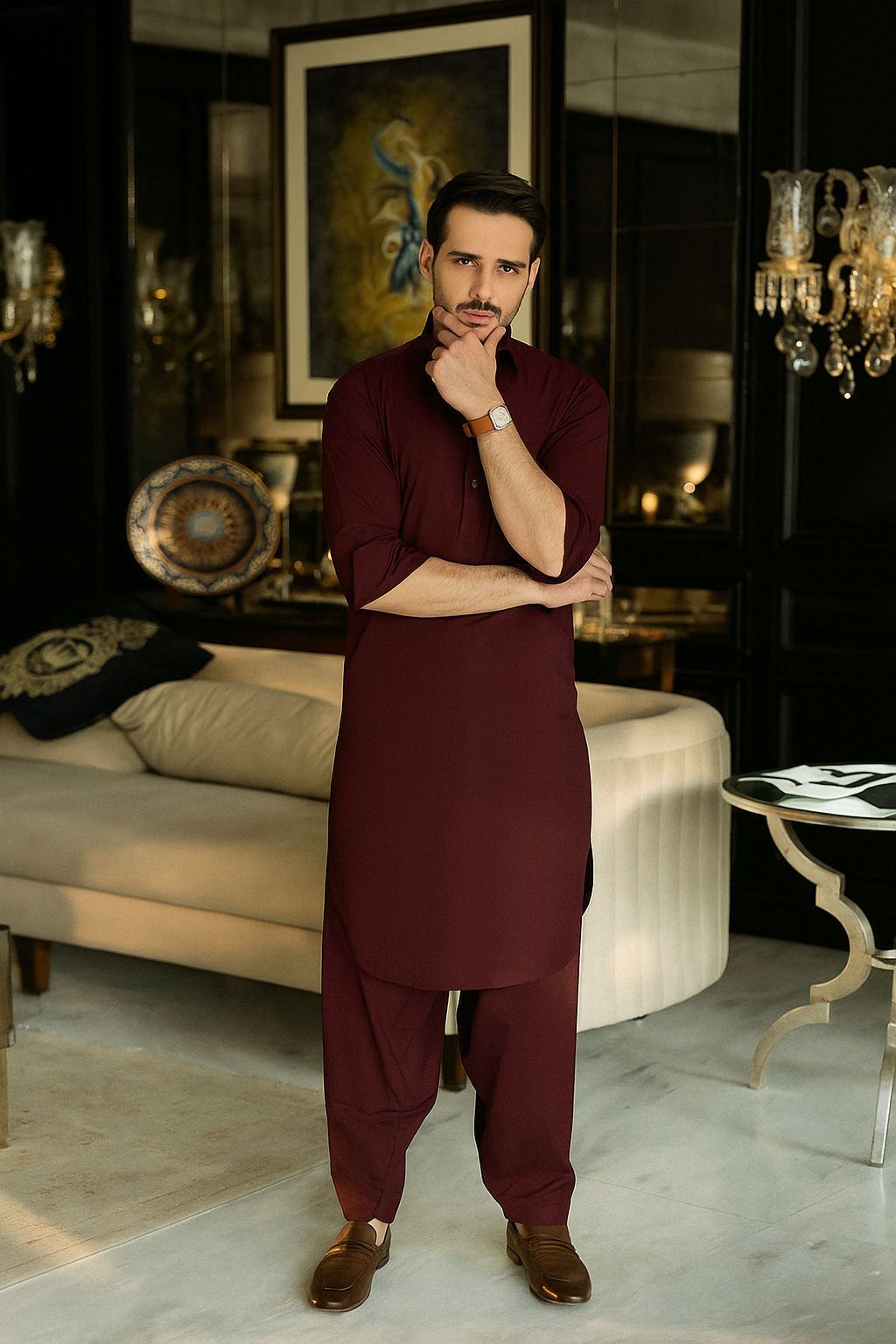 Man in maroon traditional outfit standing in a stylish room with decor elements.
