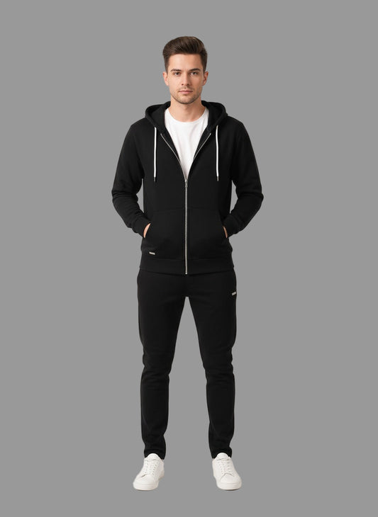 Man wearing a black hoodie and pants with white sneakers on a gray background