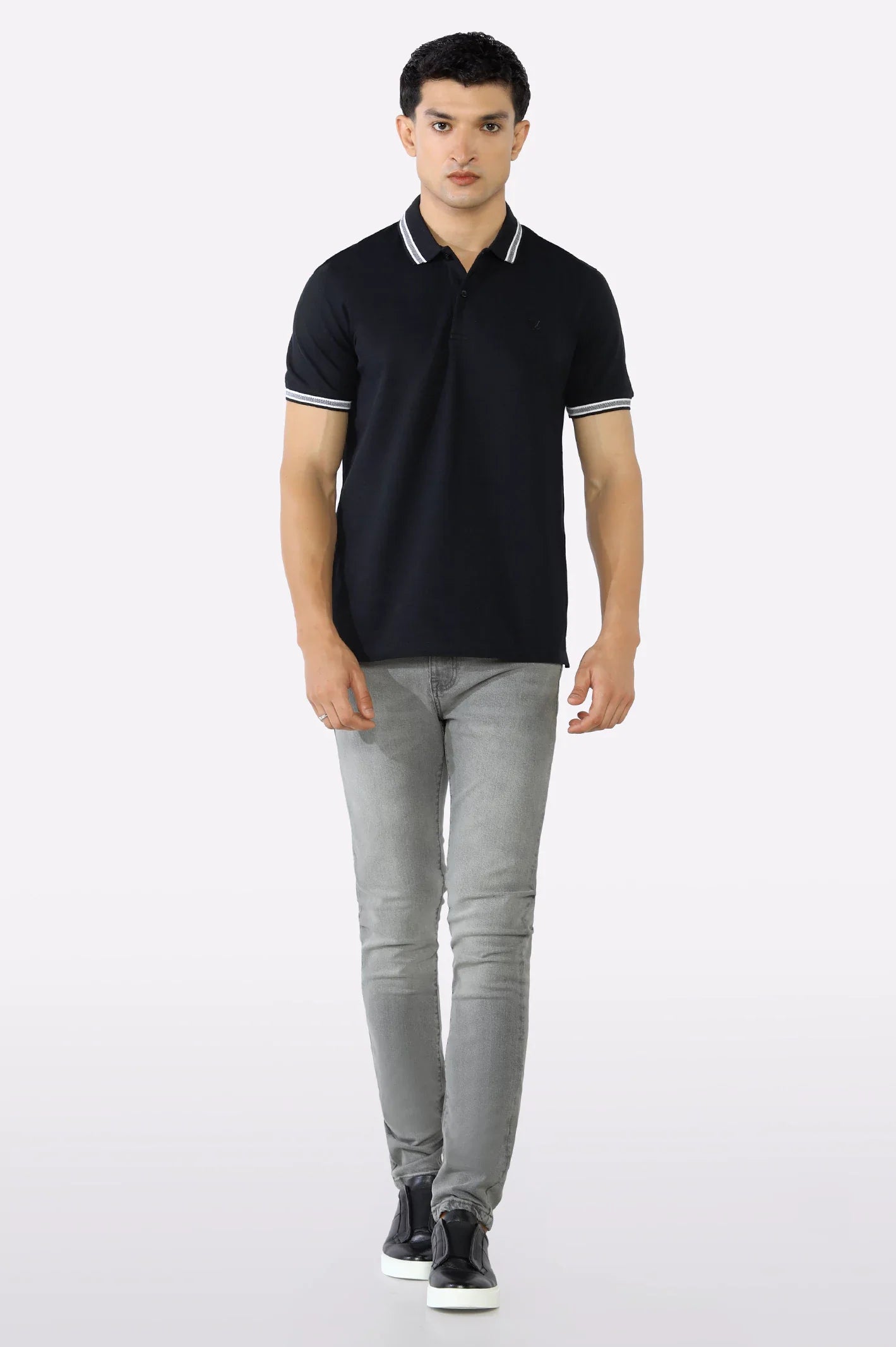 Man wearing a black polo shirt and gray jeans on a white background