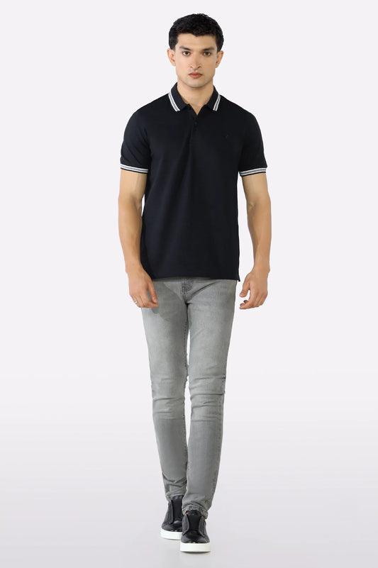 Man wearing a black polo shirt and gray jeans on a white background