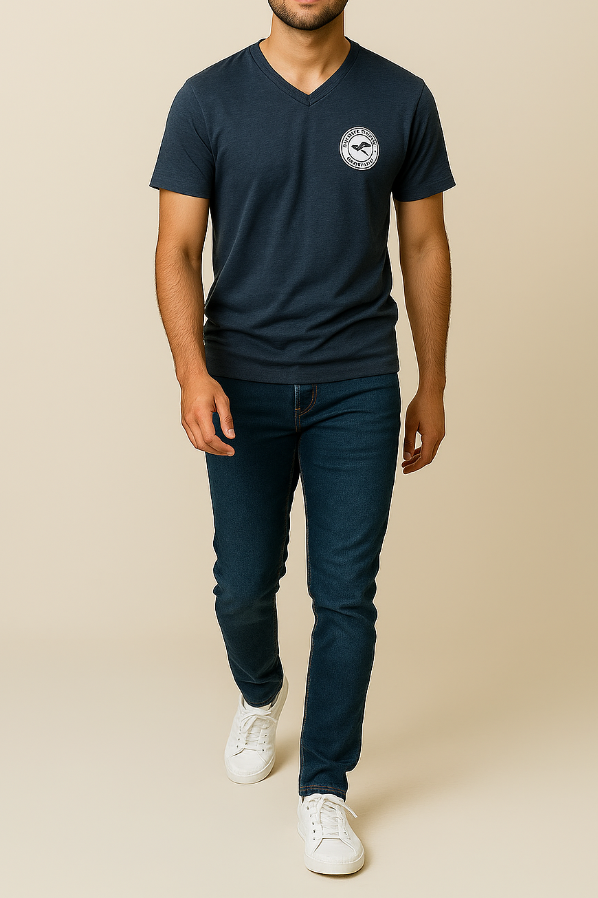 Man wearing a navy V-neck t-shirt with a logo and dark blue jeans on a beige background