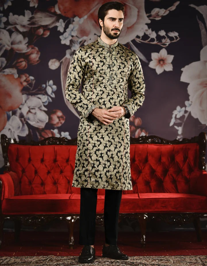 Man wearing a patterned kurta with black pants in front of a decorative floral wall and red sofa.