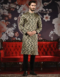 Man wearing a patterned kurta with black pants in front of a decorative floral wall and red sofa.