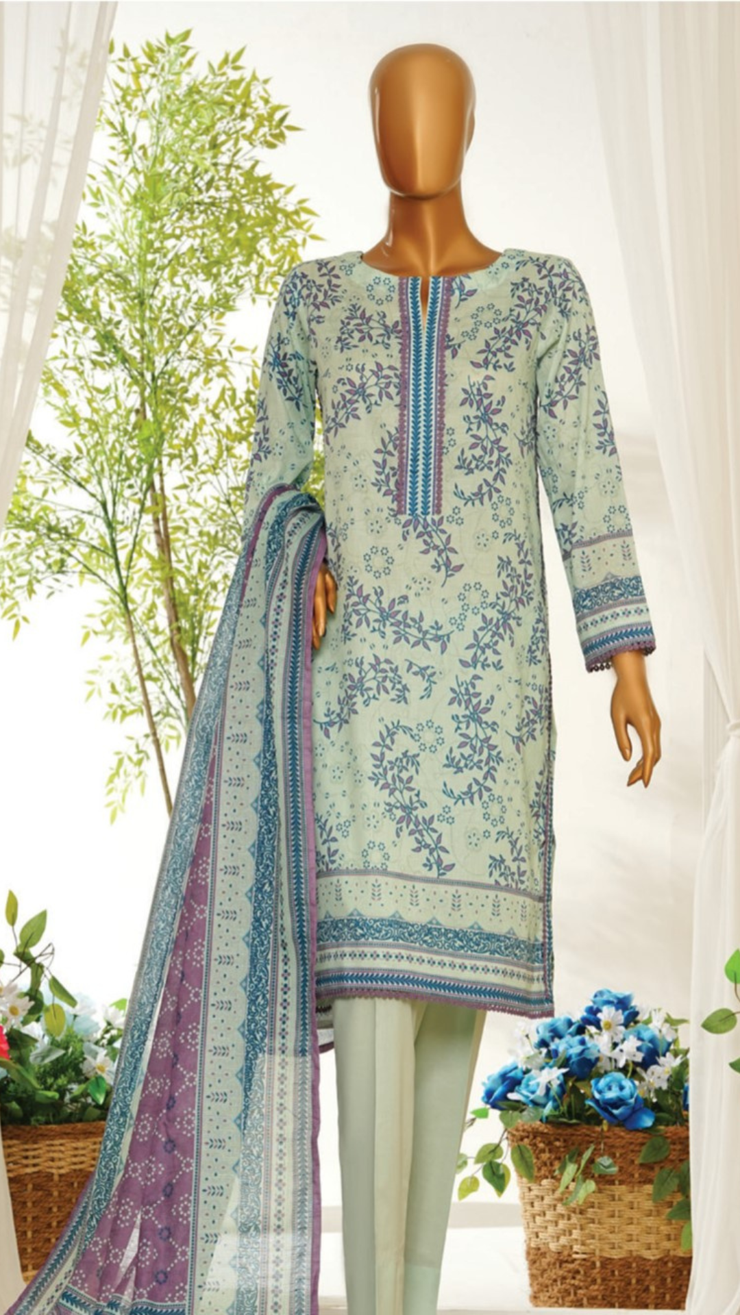Mannequin wearing MTJ  a light blue printed dress with a floral pattern, standing in a bright room with plants.