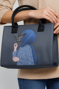 Navy blue handbag with artistic design of a person wearing a blue headscarf and holding flowers, held by a person in a beige jacket.