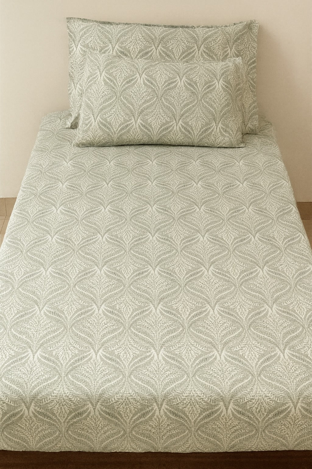 Patterned gray bedspread with matching pillow on a bed against a beige wall.