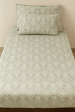 Patterned gray bedspread with matching pillow on a bed against a beige wall.