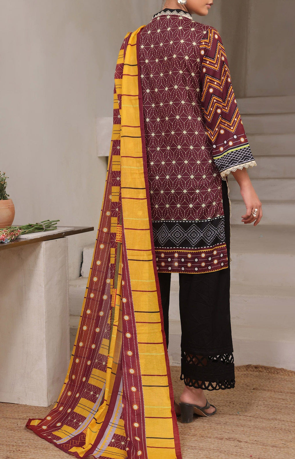 Person wearing a patterned maroon and yellow dupatta with a plain black outfit indoors.