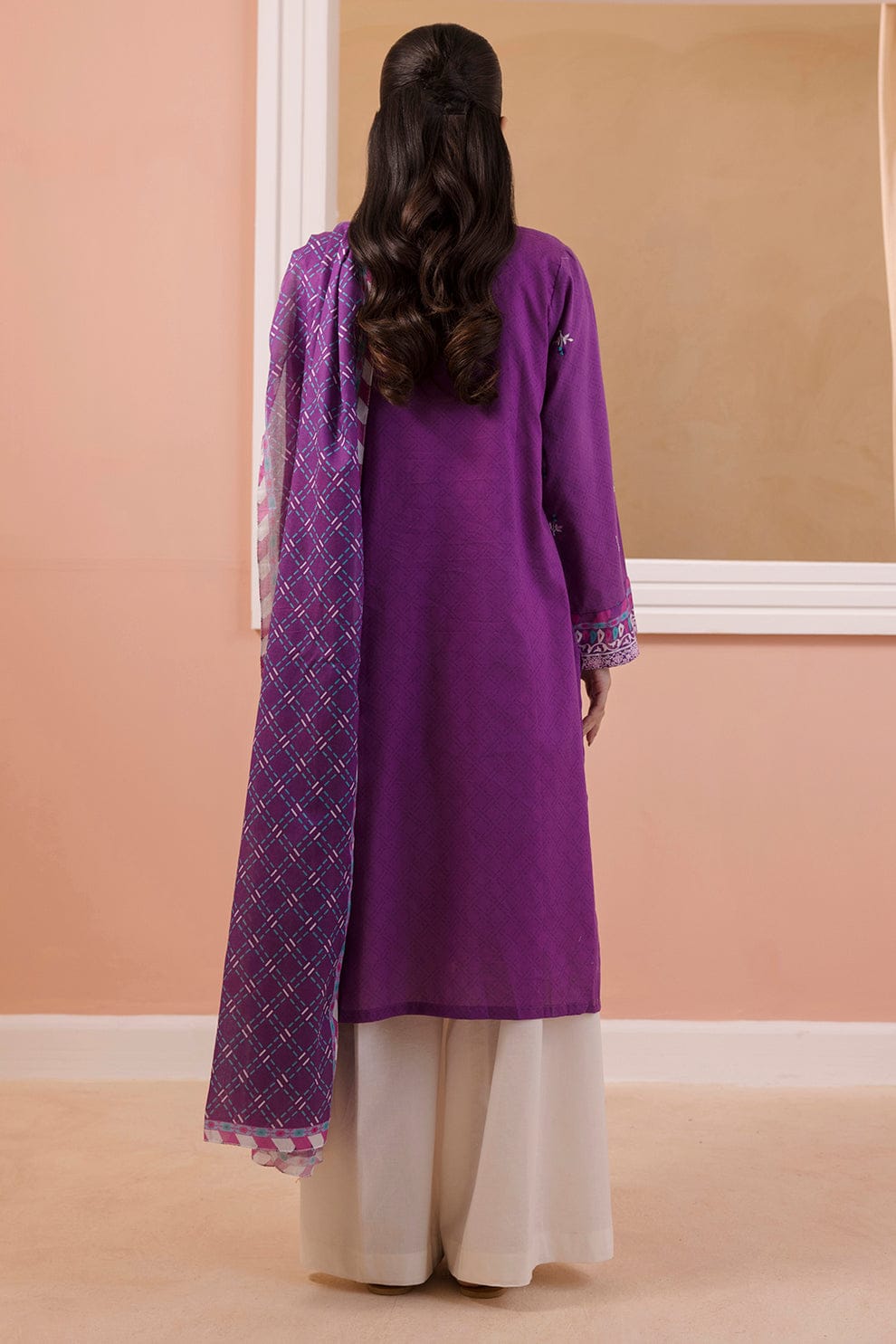 Person wearing a purple kurta with a matching dupatta against a beige wall.