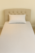 Single bed with a beige headboard and a white pillow on a plain background