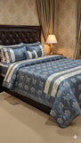 Blue and white floral patterned comforter set on a bed with matching pillows, against a beige wall.