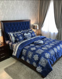 Blue patterned bedding set on a bed in a bedroom with curtains and lamps.