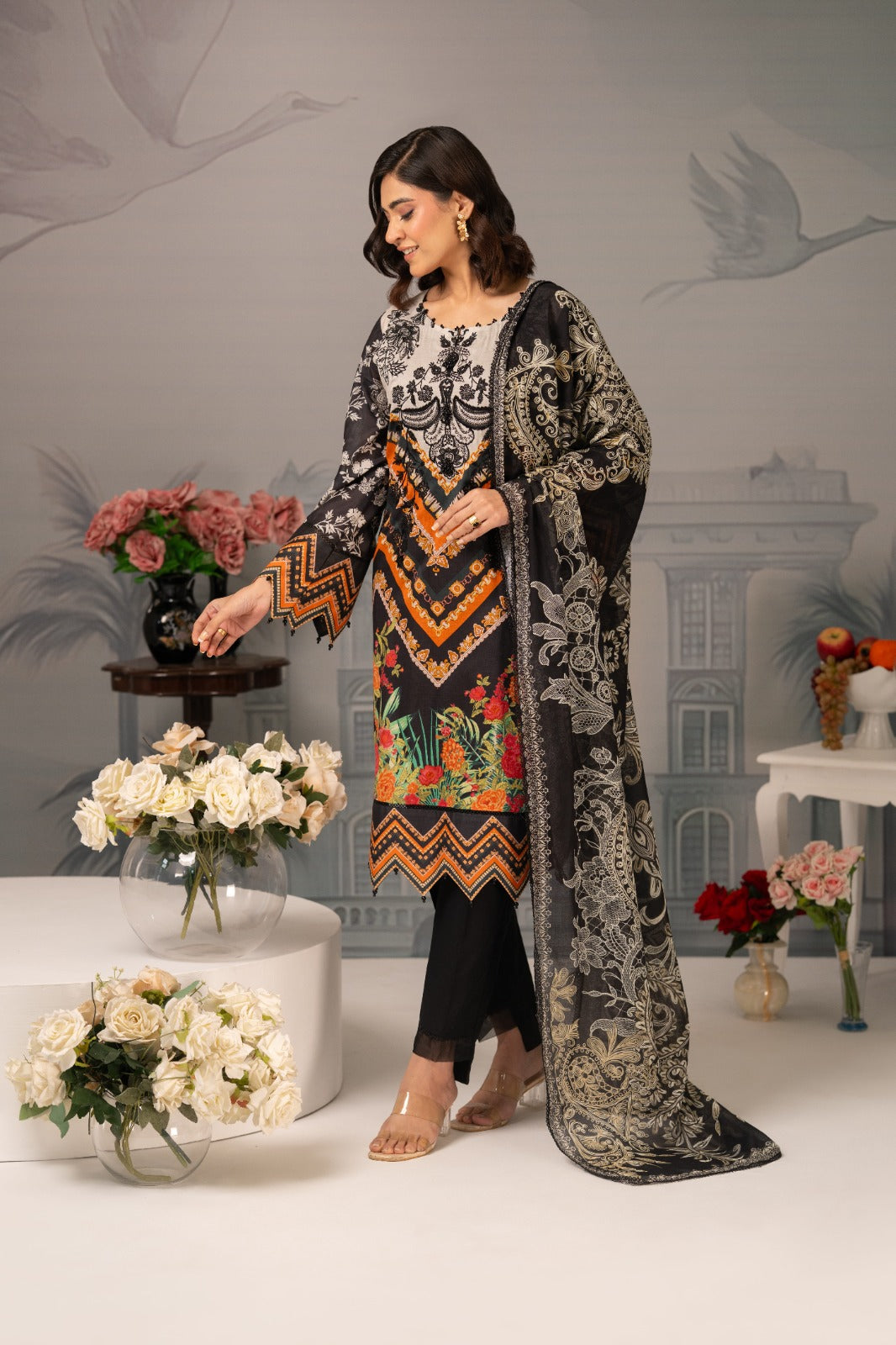 Woman in a traditional outfit with floral patterns standing in a decorated room with flowers and vases.