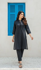 Woman wearing a black patterned outfit standing in front of a blue shutter.