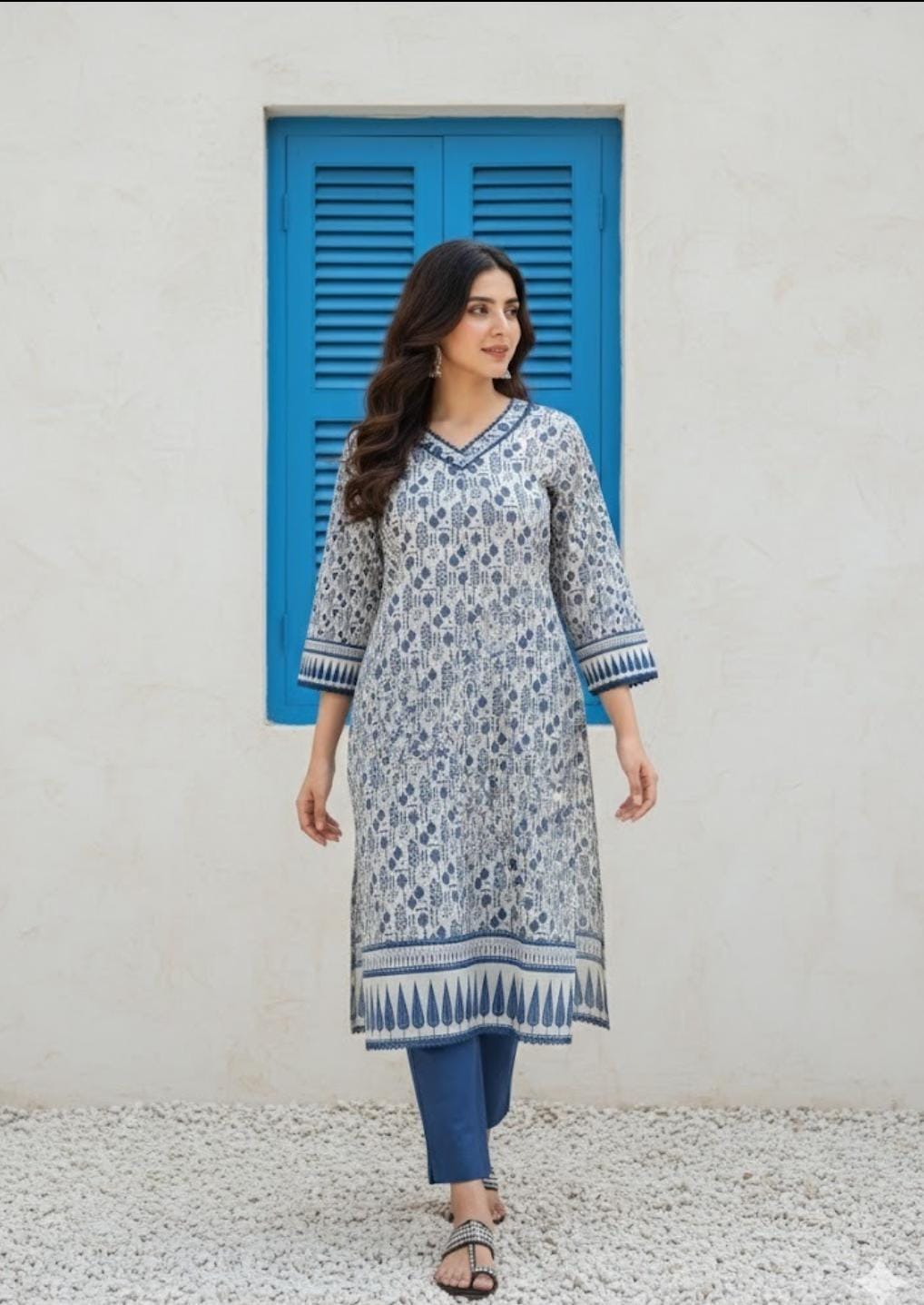 Woman wearing a blue and white patterned kurta standing in front of a blue shutter.