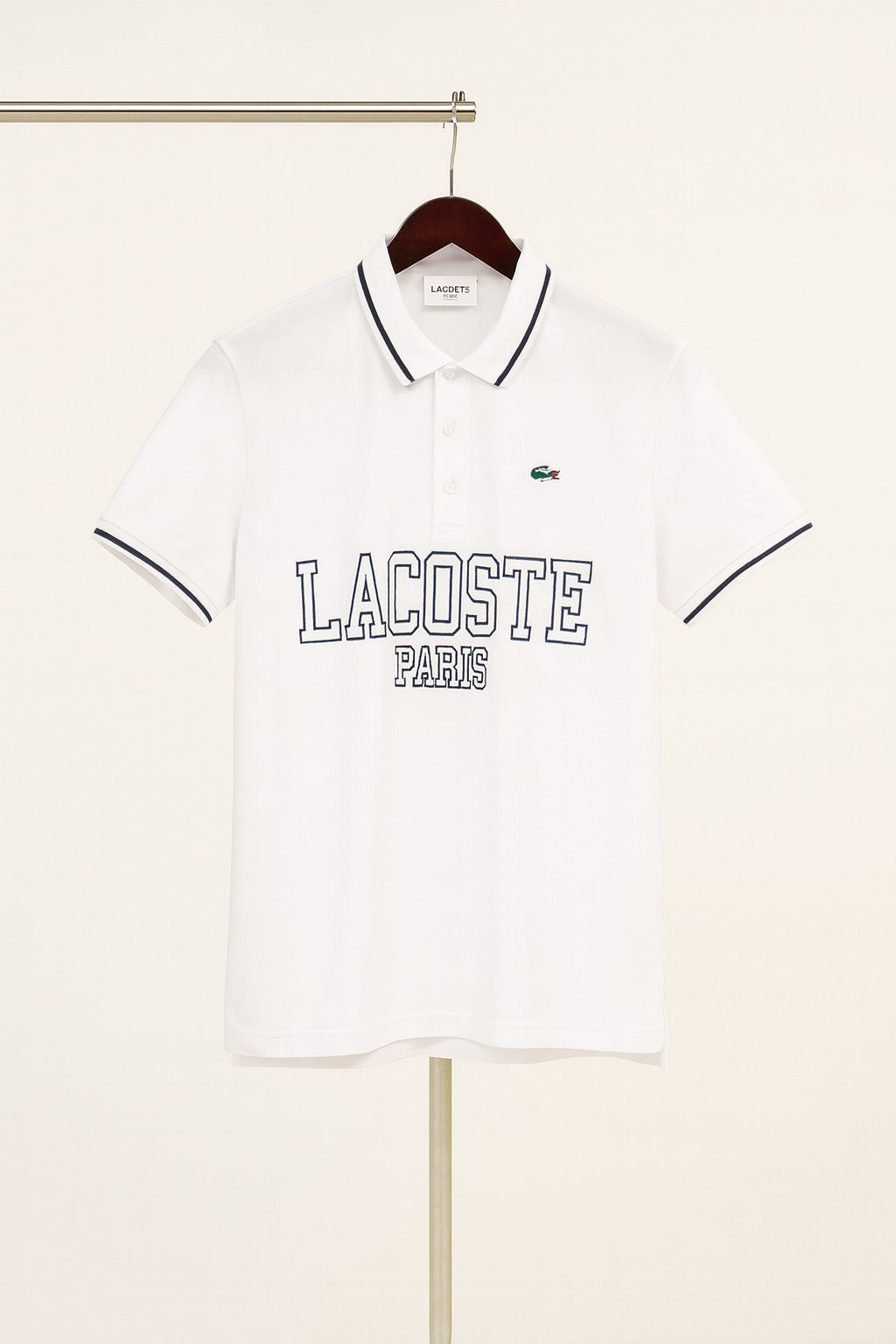 White Lacoste Paris polo shirt on a hanger against a white background