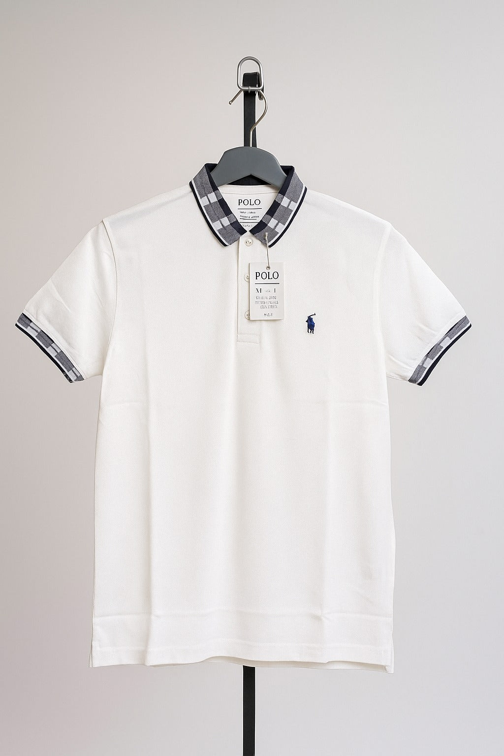 White polo shirt with plaid collar and sleeves on a hanger against a gray background