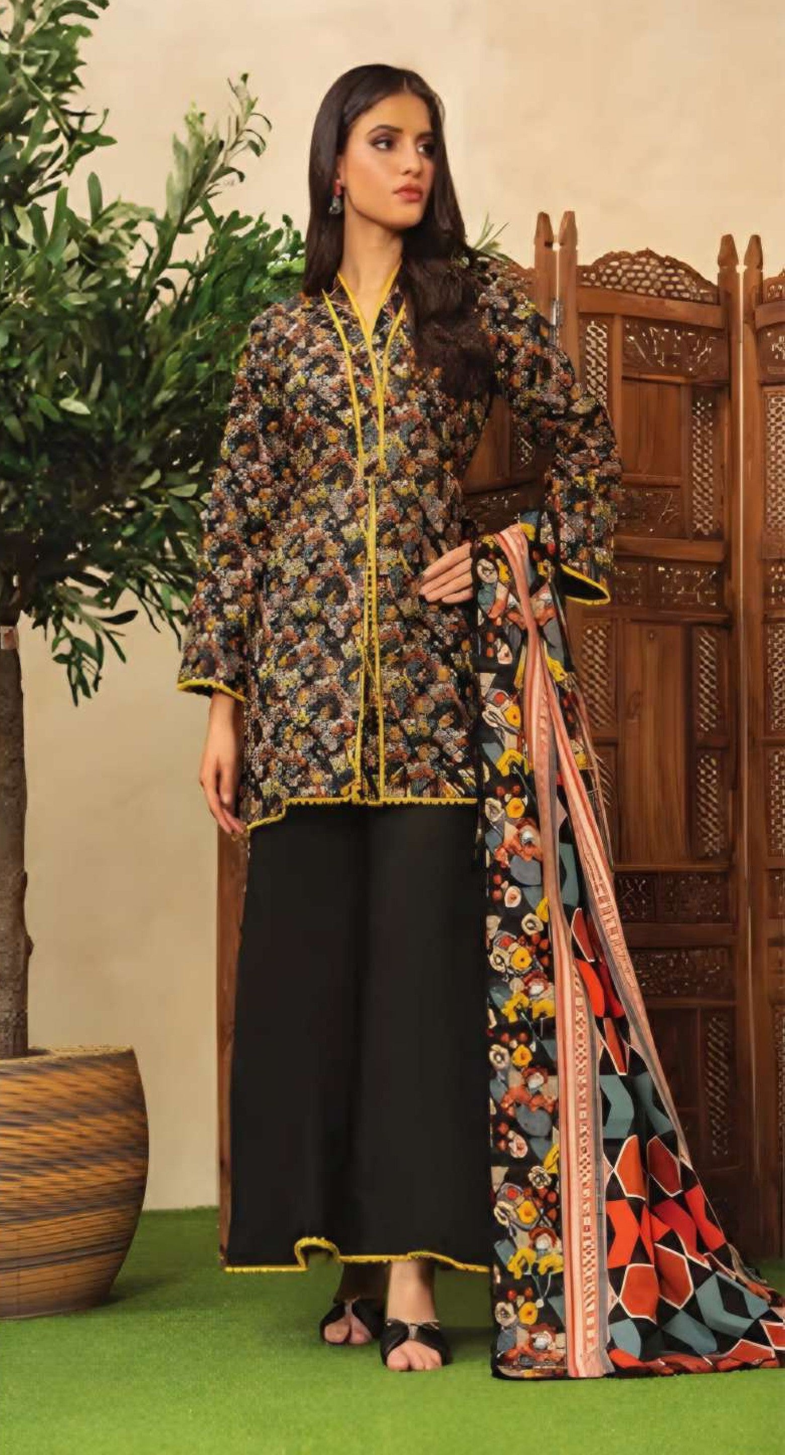 Woman holding a floral dress in a decorative setting with plants and wooden furniture.