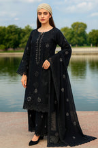 Woman in a black embroidered outfit standing by a lake with trees in the background