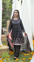 Woman in a black printed dress with a colorful dupatta, standing outdoors with white curtains and floral decorations.