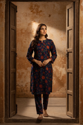 Woman in a blue patterned kurta standing in an open doorway with a textured wall behind.