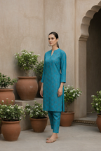 Woman in a blue traditional outfit standing in a decorative outdoor setting with plants.