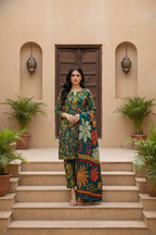 Woman in a colorful traditional outfit standing on steps with a beige wall and plants in the background