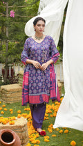 Woman in a purple and pink traditional outfit standing in a garden with flowers and greenery.