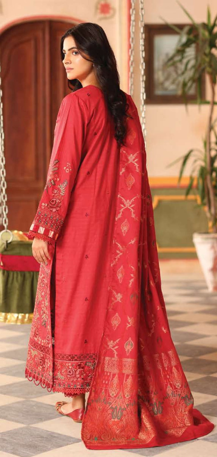 Woman in a red embroidered traditional outfit standing in a decorated room.