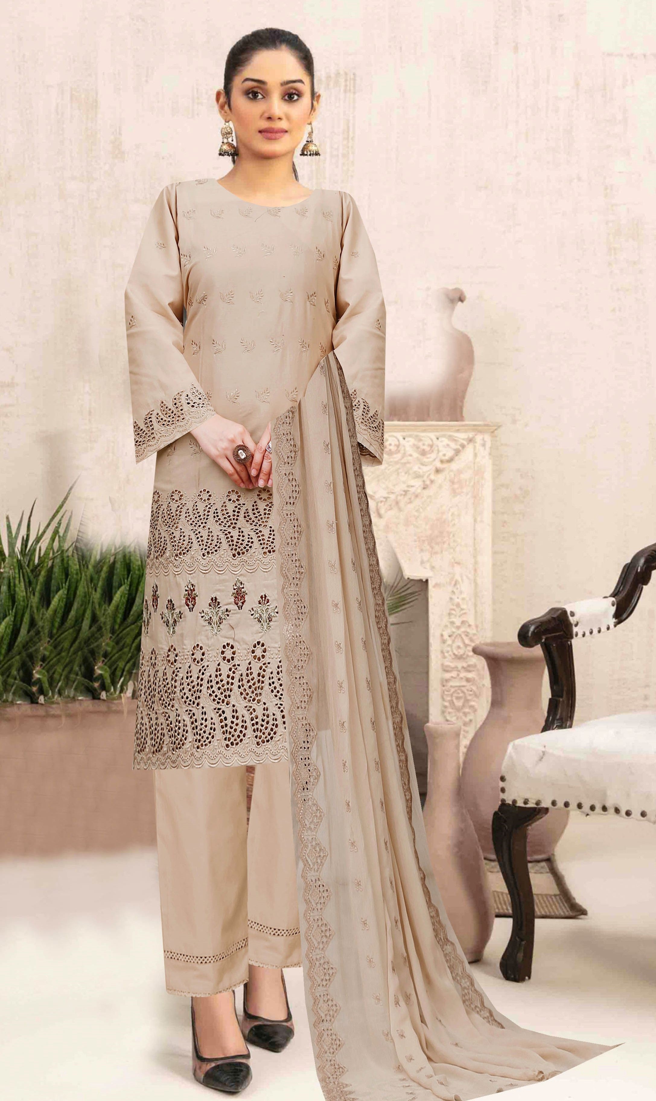 Woman wearing a beige traditional outfit with intricate patterns in a well-lit room.