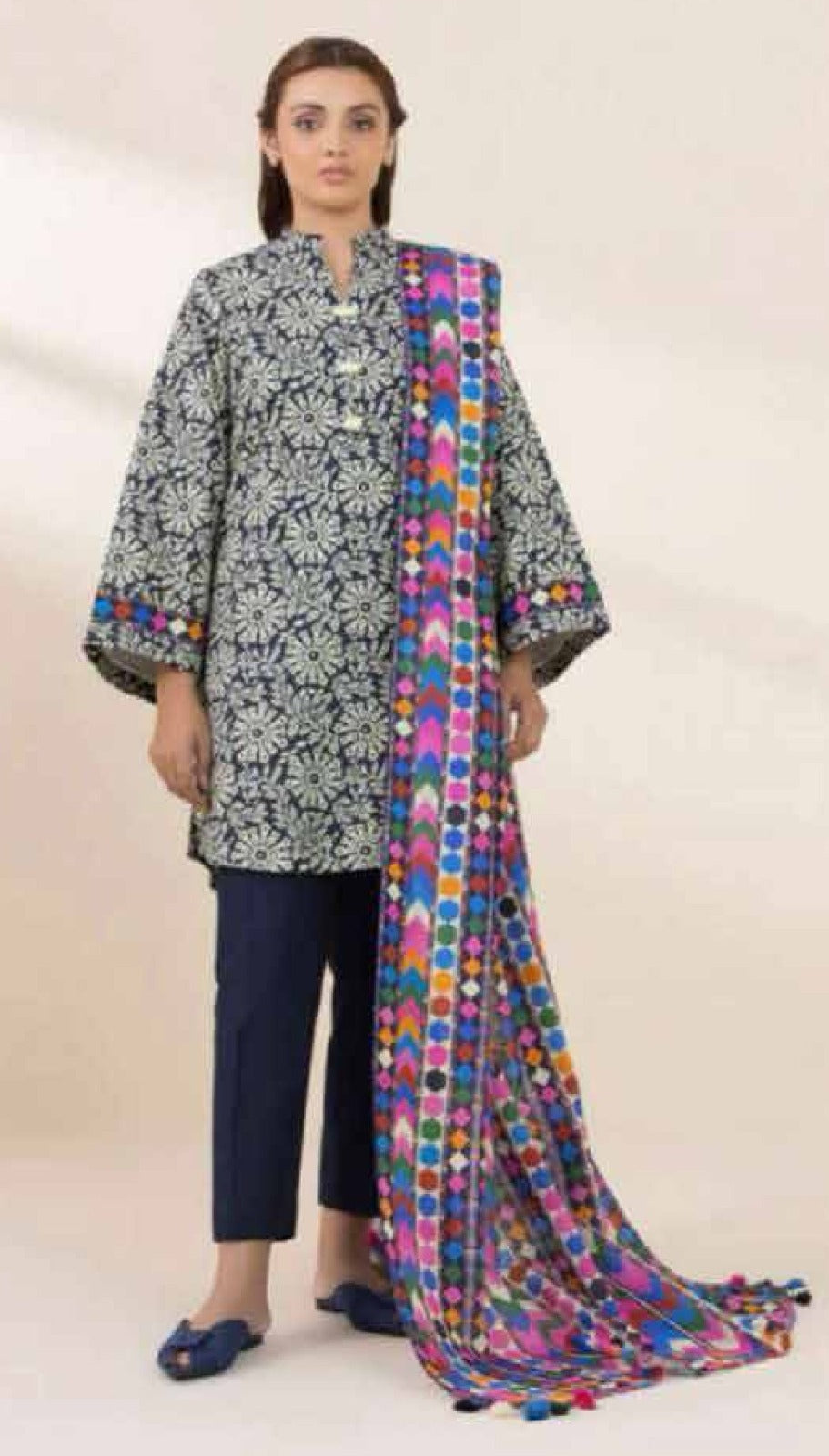 Woman wearing a black and white patterned kurta with navy pants and a colorful dupatta on a beige background